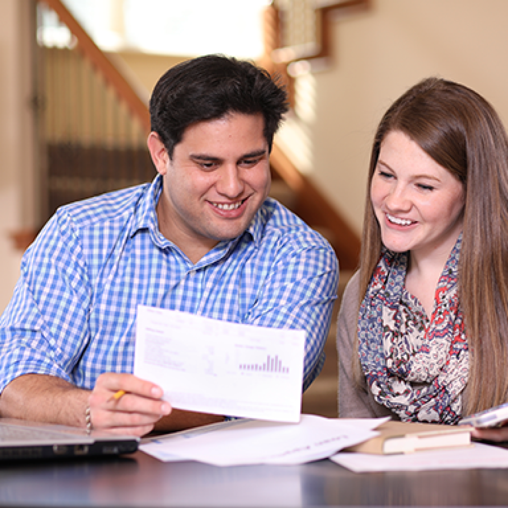 woman and man sitting down looking at a white card that is a water bill inside their home