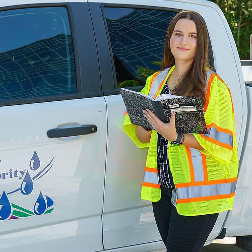 Image of female engineer with notebook by work vehicle. 