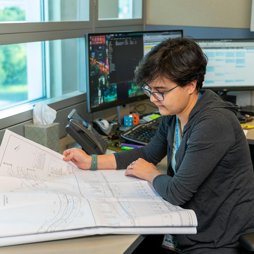 Image of woman looking at plans in an office setting. 