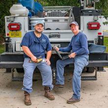 Image of two male lift station workers sitting on the back end of their truck